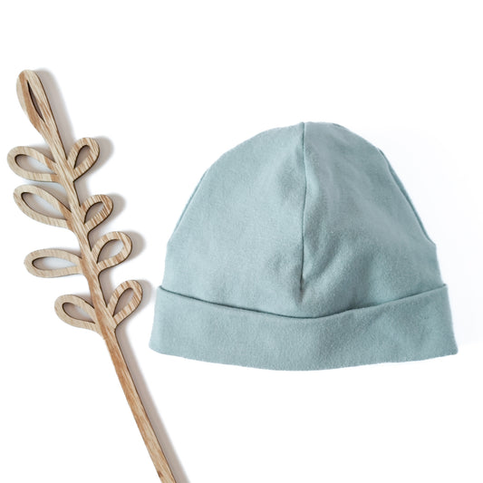 Vorderansicht einer Beanie mit Umschlag in der Farbe blau neben Dekoblume aus Holz