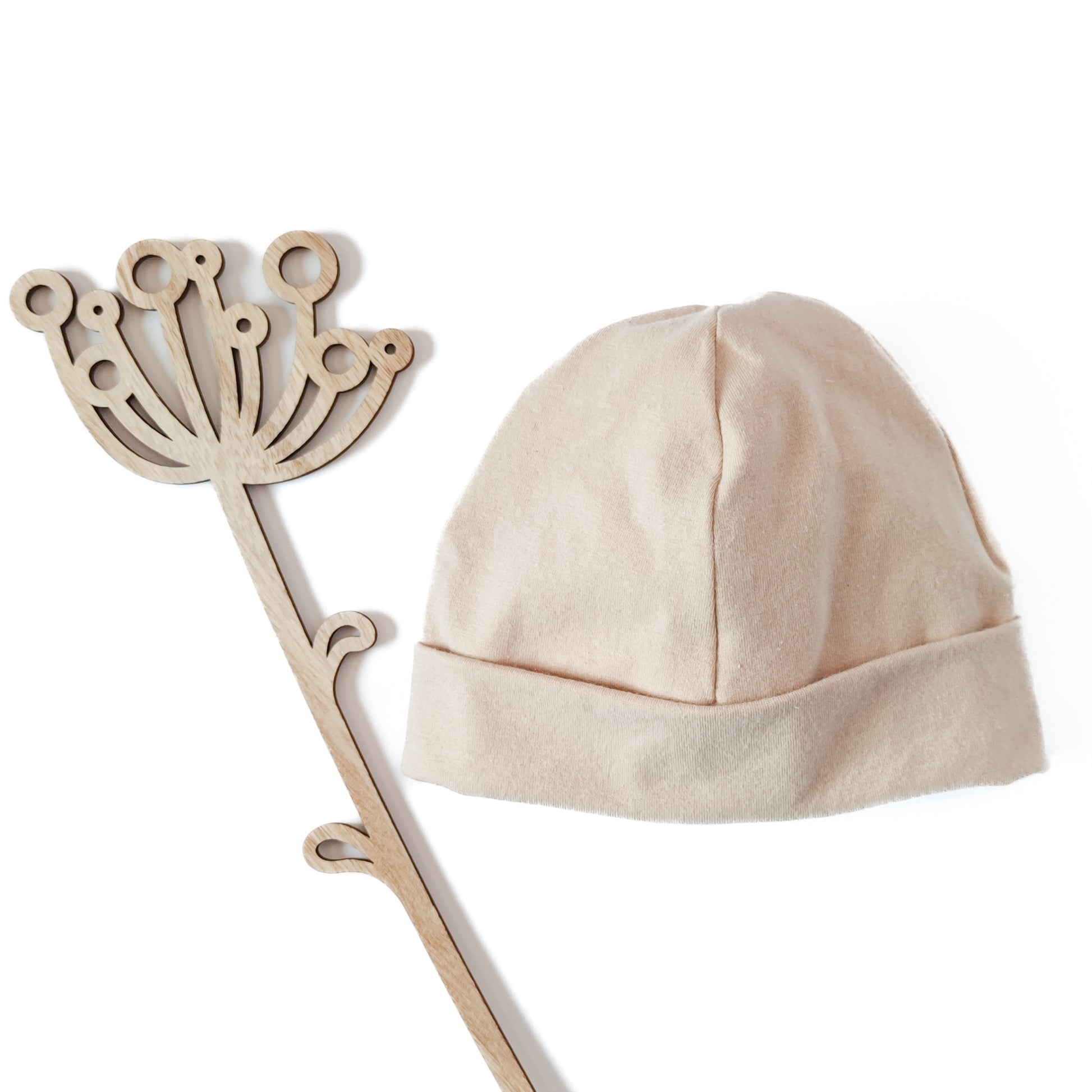 Vorderansicht einer Beanie mit Umschlag in der Farbe beige neben Dekoblume aus Holz