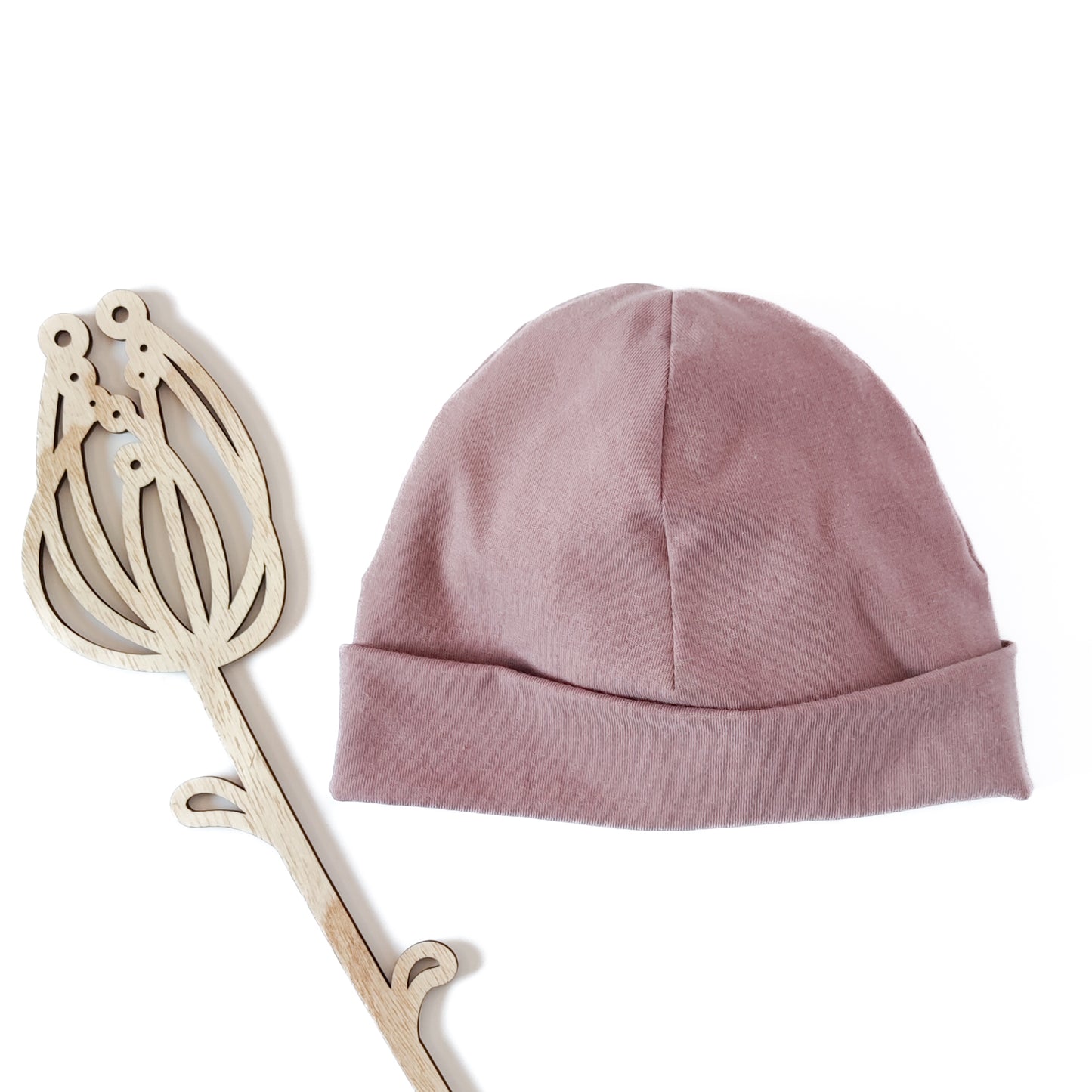 Vorderansicht einer Beanie mit Umschlag in der Farbe rosa neben Dekoblume aus Holz